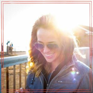 Mira Goto wearing sunglasses, smiling with sun shining in background.