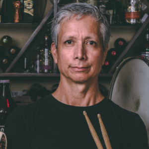Headshot of Robonzo, Host of The Unstarving Musician, wearing black tee, holding drumsticks
