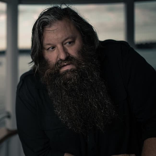 Bradford Loomis in dark shirt leaned and looking to one side with a curious expression.