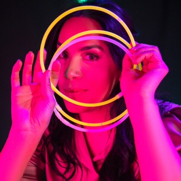 Recording artist Amiena lit in pink holding neon glow circles in front of face, representing halos