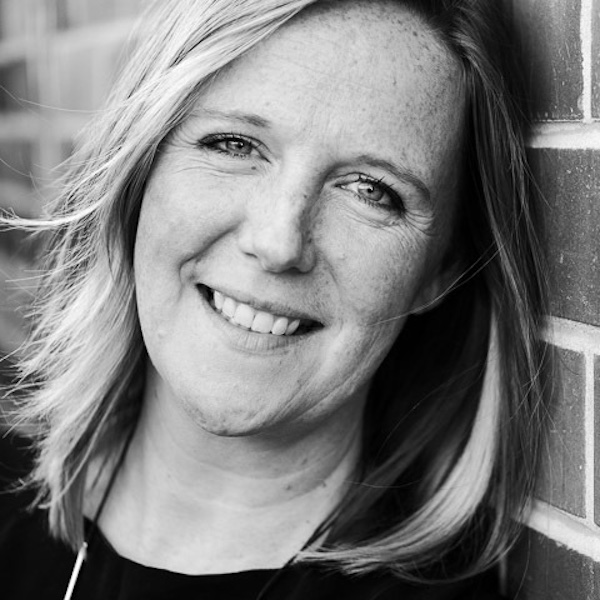 Lynz Crichton, musician and creator of Music Marketing Method, black & white headshot leaning against brick wall, smiling