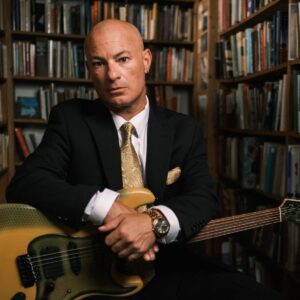 Ryan Rosoff of Little King sitting in library with guitar in suit and tie