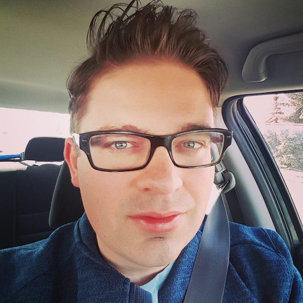 David Andrew Wiebe, headshot wearing dark rimmed glasses in car with seatbelt