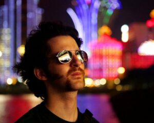 Zack O'Malley Greenburg, standing in colorful night city scape, wearing sunglasses