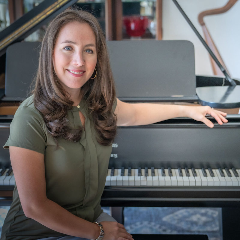 Fabiana Claure sitting at a black piano facing camera