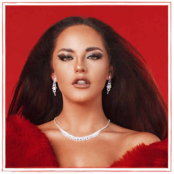Fia Nyxx on red background, wearing red and diamond earrings & necklace. Fia Nyxx – PR, Marketing, Common Indie Artist Struggles, Video Collaboration, Release Strategy, Recording Studio Lessons, Confidence Through Repetition, And Theatrical Performance