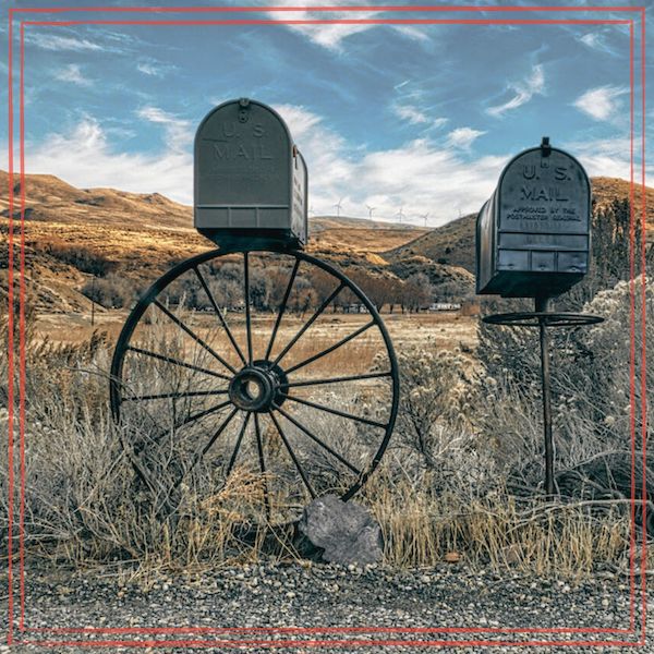 Mailboxes on a countryside road with a field and sky backdrop.