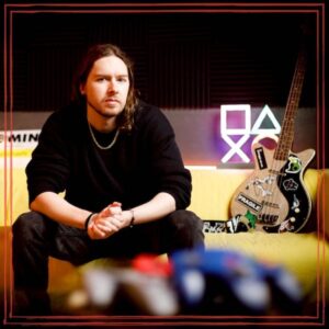 Unstarving Musician Episode Artwork featuring Timothy Reid sitting in studio w/guitar and game controller nearby