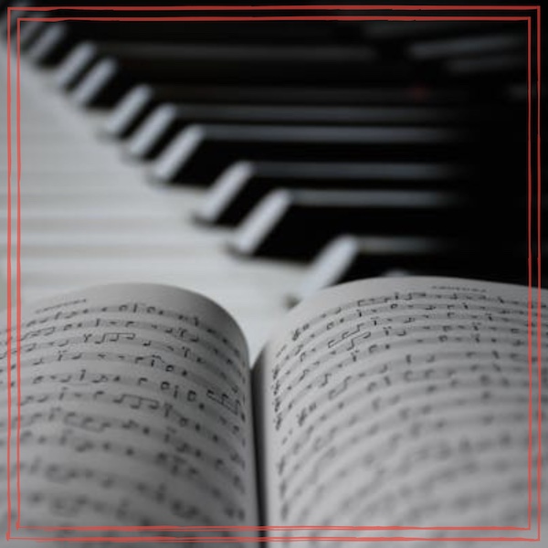 An open music book of sheet music in the foreground, with piano keys receding into the background at an angle