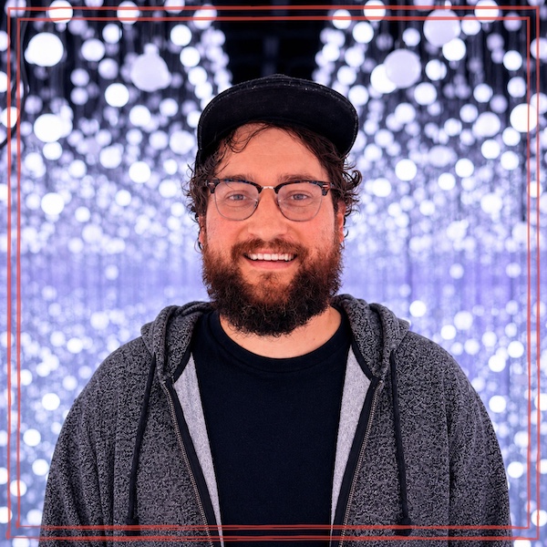 Cody Delong in a ball cap and hoodie against a background of lavender sparkling lights.