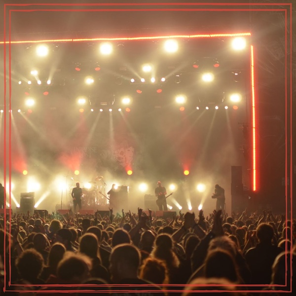 Concert venue with a packed crowd facing a brightly lit stage framed by warm amber and white lights.